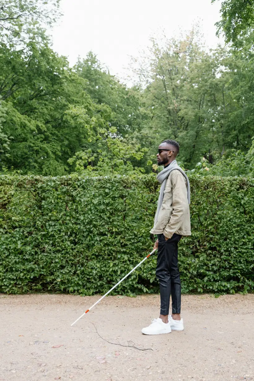 A blind man walking with a white cane along a hedge