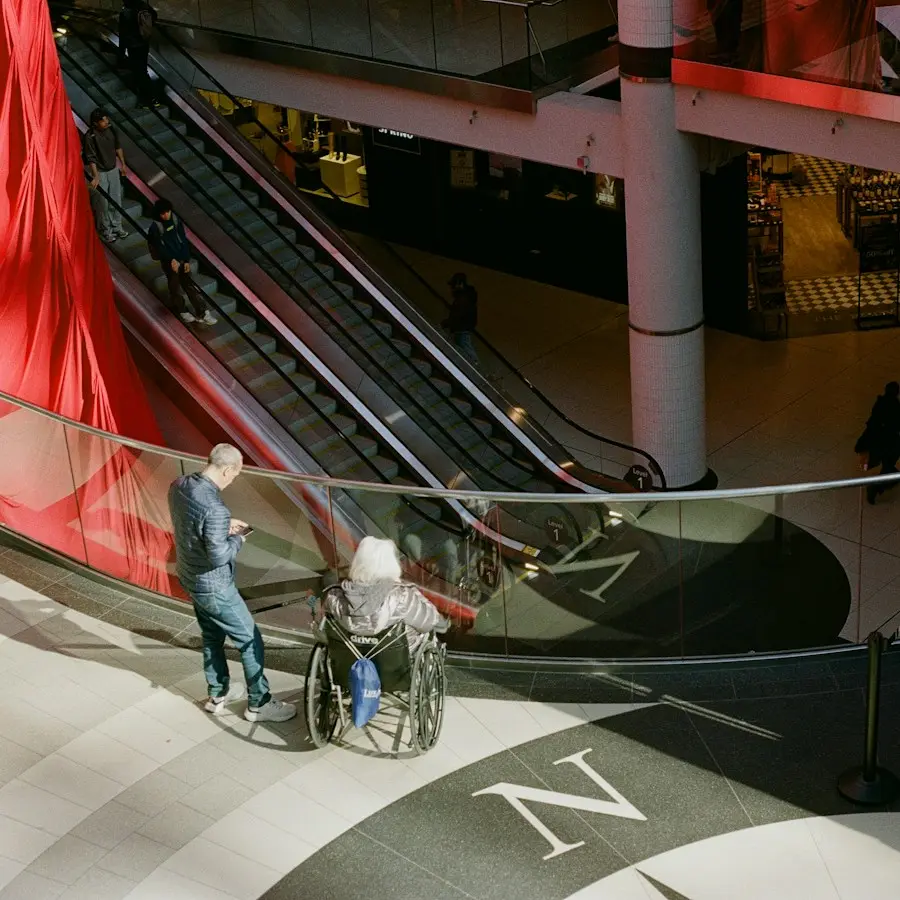Wheelchair user and shoppers on the escalators of a mall
