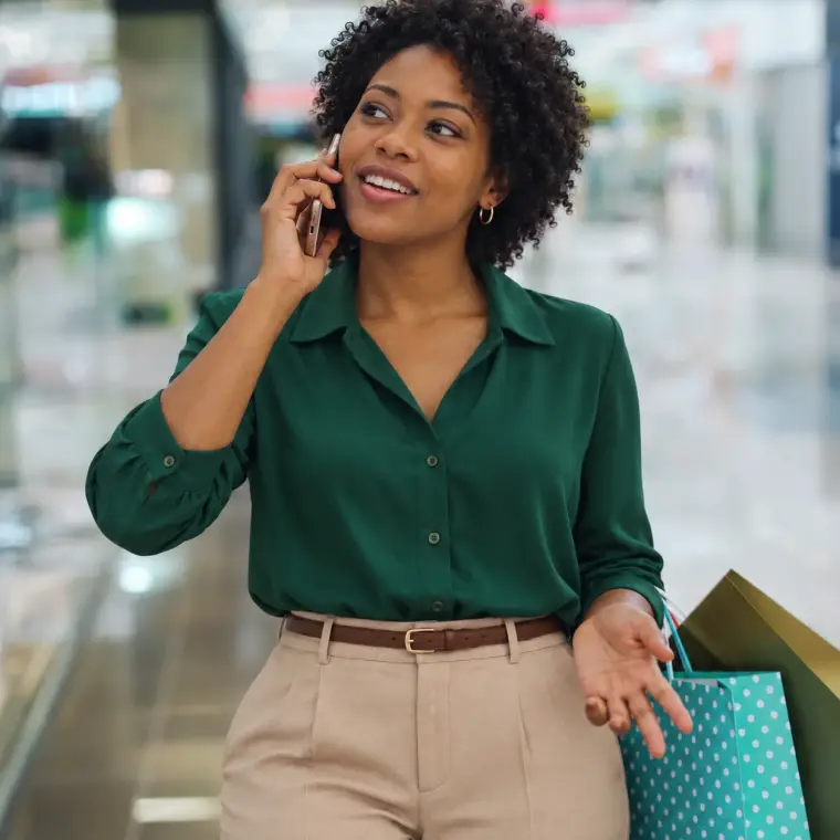 Smiling shopper with bags talking on her phone in a mall