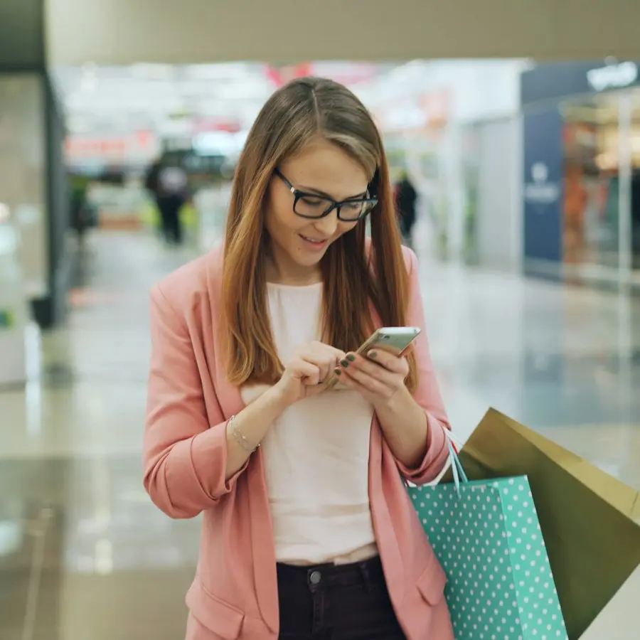 Smiling shopper checking her phone while holding shopping bags
